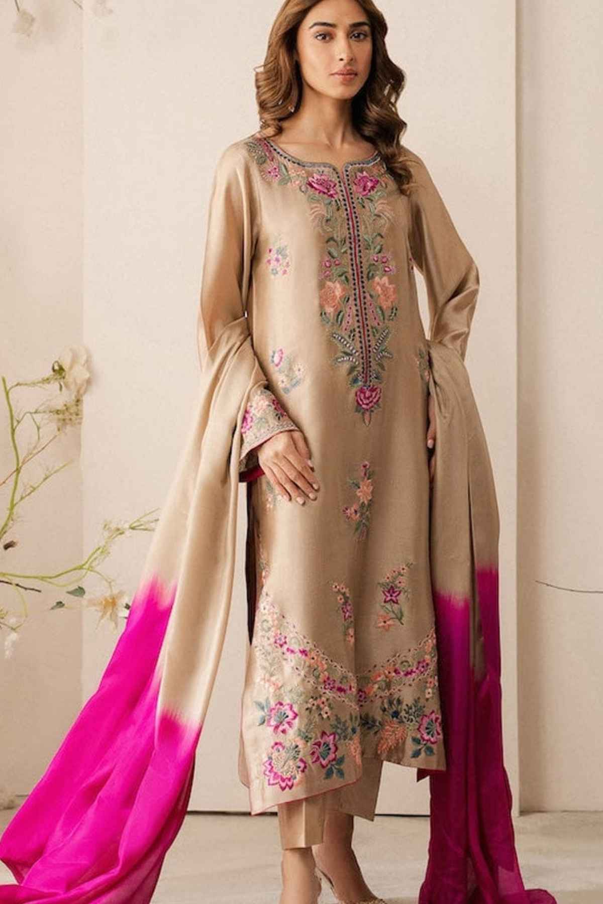 Woman wearing a beige embroidered dress with pink dupatta against a neutral background