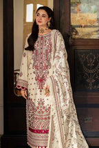 A woman models a traditional three-piece salwar kameez suit in cream with intricate red and gold embroidery, standing in an elegant indoor setting with dark wood paneling.