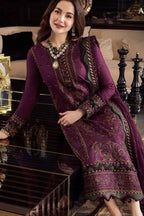 A woman models a deep purple ethnic three-piece suit with intricate gold embroidery and green accents, posing in a luxurious indoor setting.