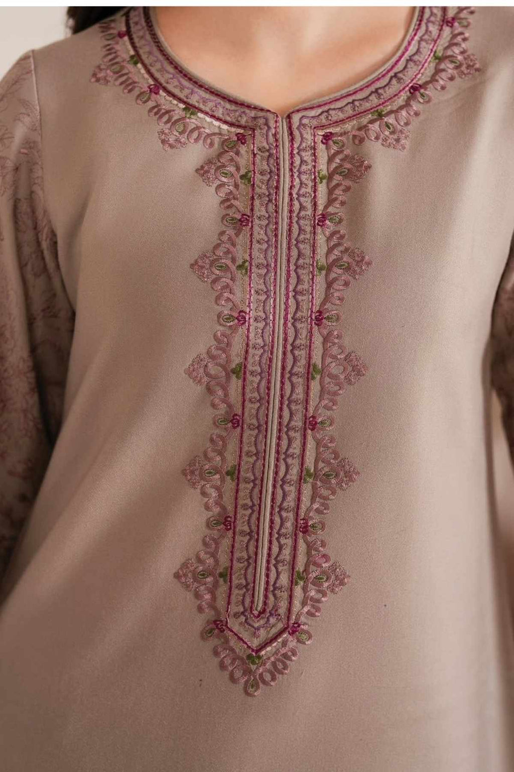 Close-up of a beige or taupe embroidered tunic top with ornate pink and green thread detailing around the neckline and down the center front.