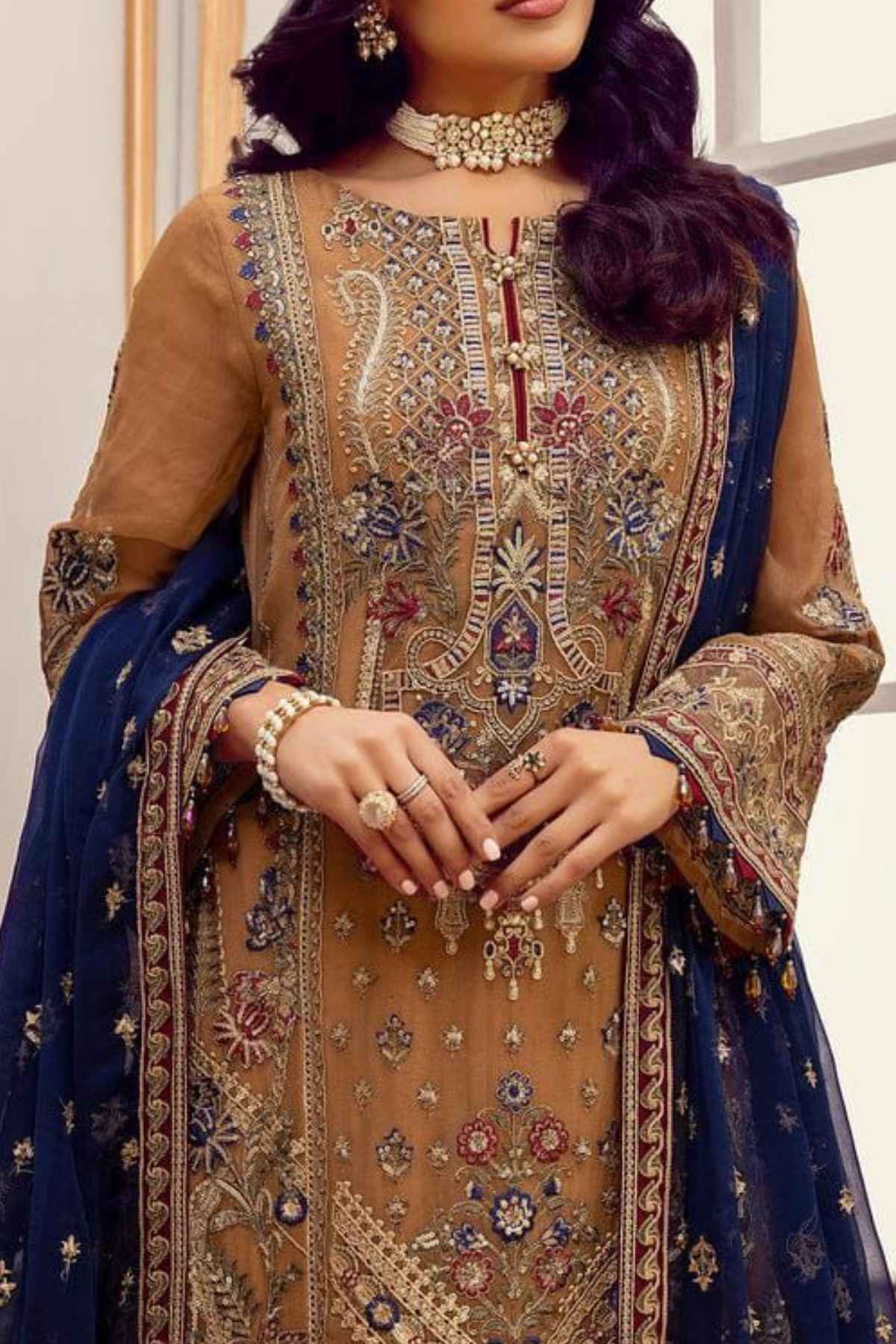 Woman wearing a traditional embroidered outfit with a blue dupatta.