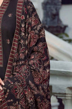 A close-up of a dark charcoal black fabric garment with intricate red, brown, and beige floral embroidery and a striped border, worn by a model in an outdoor setting.
