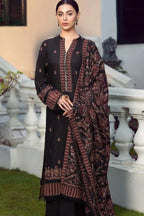 A woman models a traditional black three-piece salwar kameez suit with brown and gold embroidery, featuring a matching printed dupatta, set against an outdoor architectural background with white balustrades.
