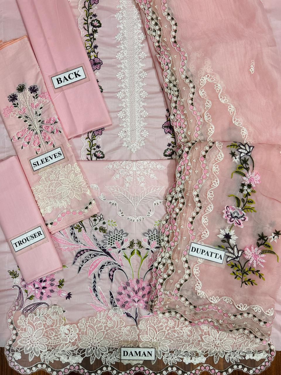Pink embroidered fabric set with labels for dhoti, dupatta, and sleeves on a pink background.