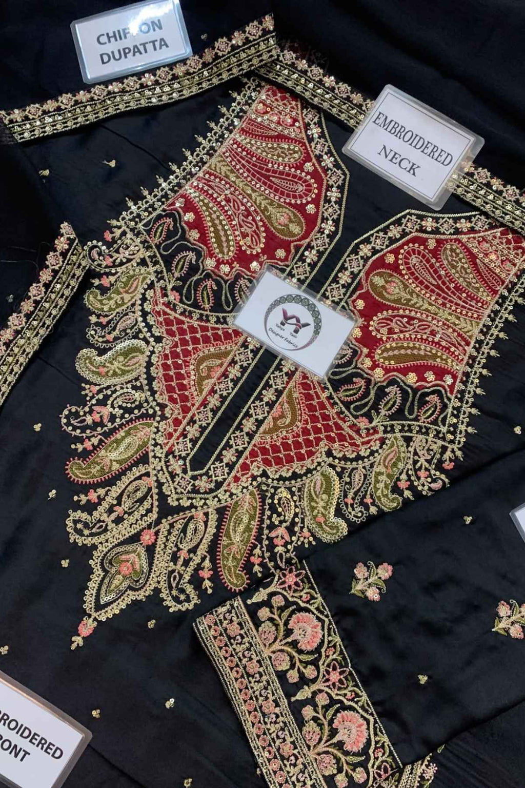 Black embroidered choli top with red paisley neckline, gold and pink floral embroidery, and multiple fabric labels showing details like 'CHIP ON DUPATTA' and 'EMBROIDERED NECK'.