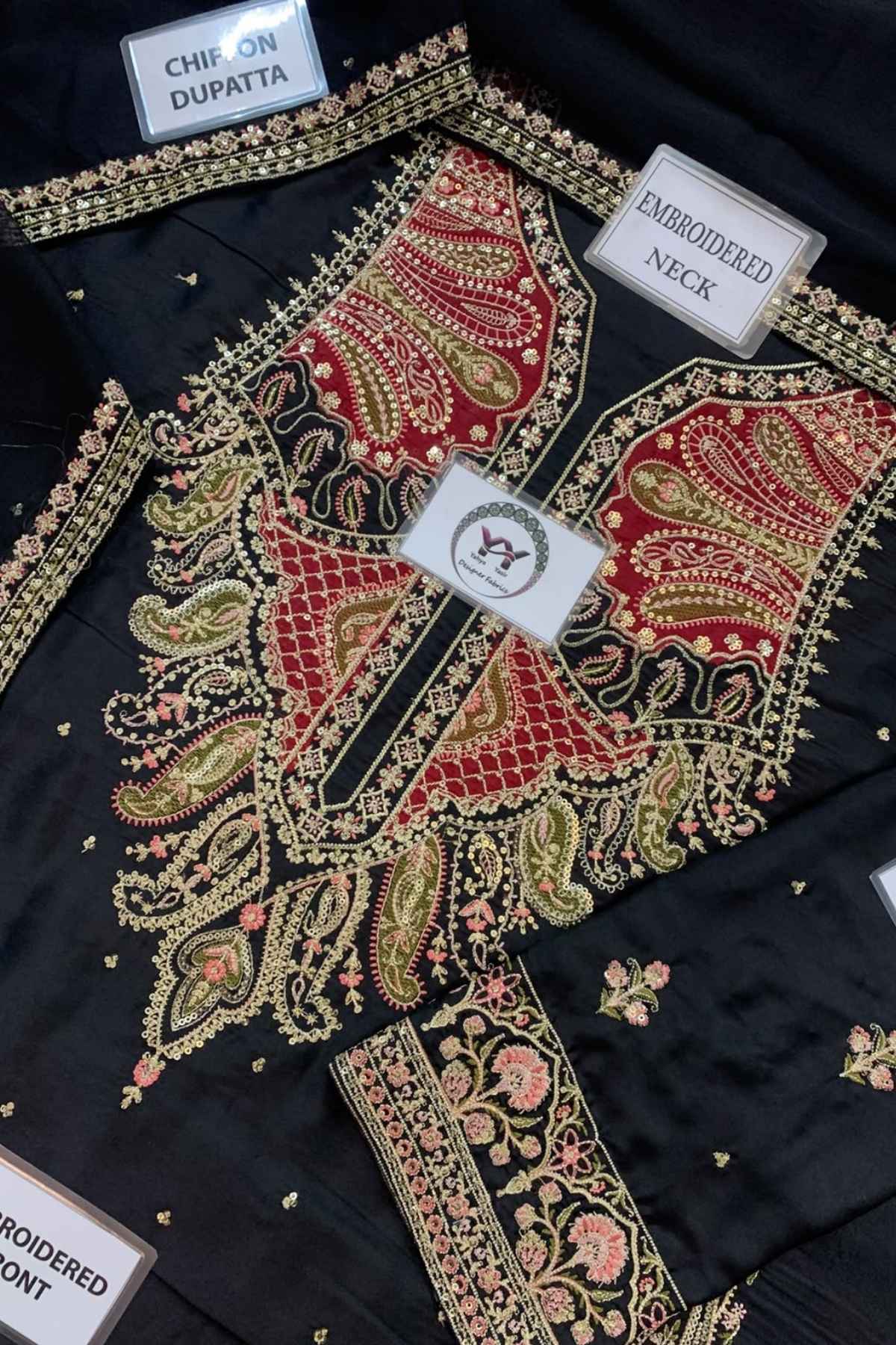 Black embroidered choli top with red paisley neckline, gold and pink floral embroidery, and multiple fabric labels showing details like 'CHIP ON DUPATTA' and 'EMBROIDERED NECK'.