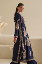 A woman modeling a navy blue traditional outfit with intricate gold paisley embroidery and embellished borders, standing in a neutral indoor setting.