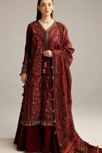 A woman models a traditional South Asian outfit consisting of a deep maroon embroidered kurta, matching trousers, and a coordinating patterned dupatta, set against a plain light gray studio background.