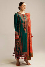 A woman modeling a traditional South Asian outfit consisting of a dark green kurta with intricate red and gold embroidery, matching trousers, and a red dupatta with gold patterns, set against a plain light gray studio background.