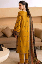 A woman modeling a mustard yellow three-piece salwar kameez suit with black printed motifs and a matching patterned dupatta in a living room setting.