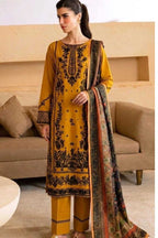 A woman models a three-piece mustard yellow ethnic suit with black floral embroidery, matching trousers, and a patterned dupatta in a living room setting.
