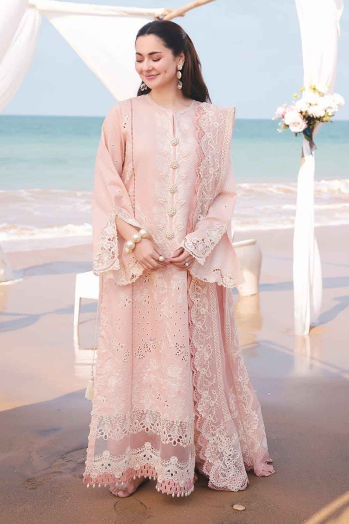 Woman in a pink lace outfit standing on a beach with ocean view