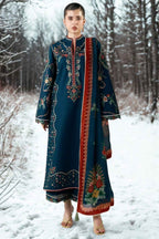 A woman stands in a snowy outdoor setting wearing a long dark teal embroidered kurta with ornate multicolor floral and geometric patterns and a red border panel.