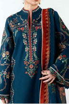 A close-up of a model wearing a dark teal embroidered kurta with floral patterns and a wide red border, paired with a matching dupatta.
