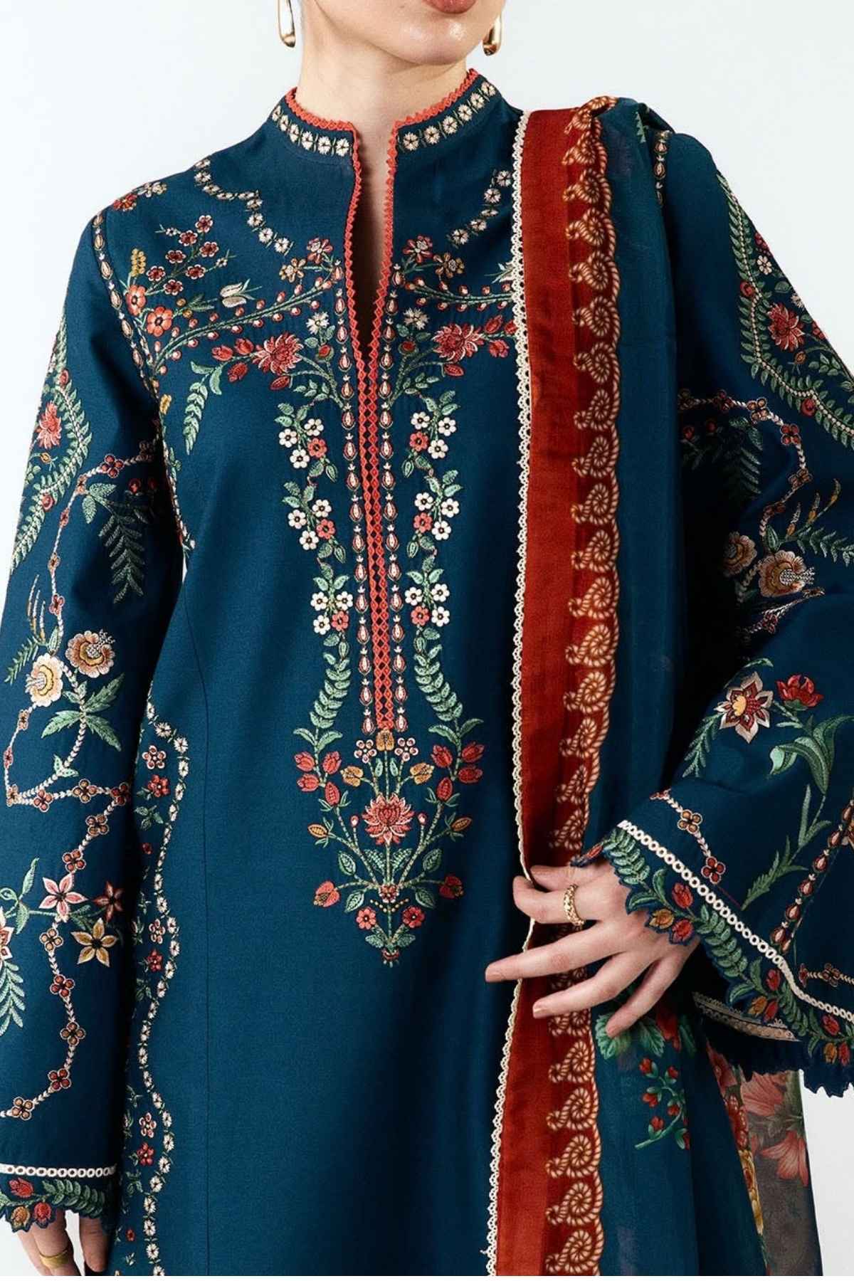 A close-up of a model wearing a dark teal embroidered kurta with floral patterns and a wide red border, paired with a matching dupatta.