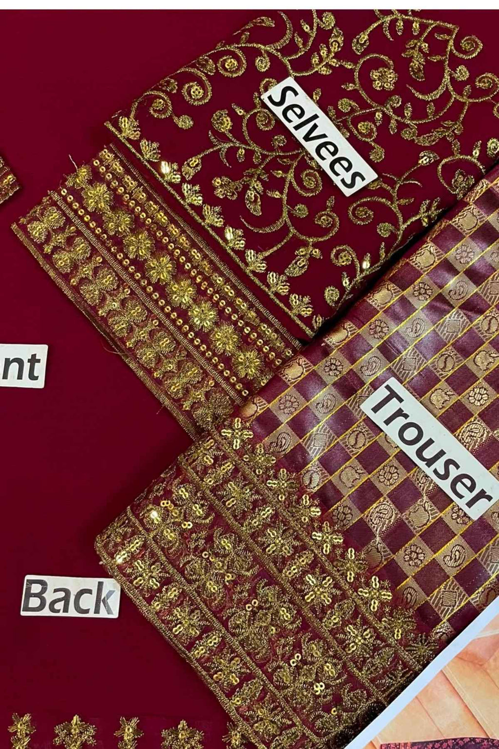 A close-up of a maroon and gold embroidered fabric set labeled with parts: 'Sleeves', 'Trouser', and 'Back'. The fabric features intricate gold floral embroidery and checkered patterns on a deep maroon background.