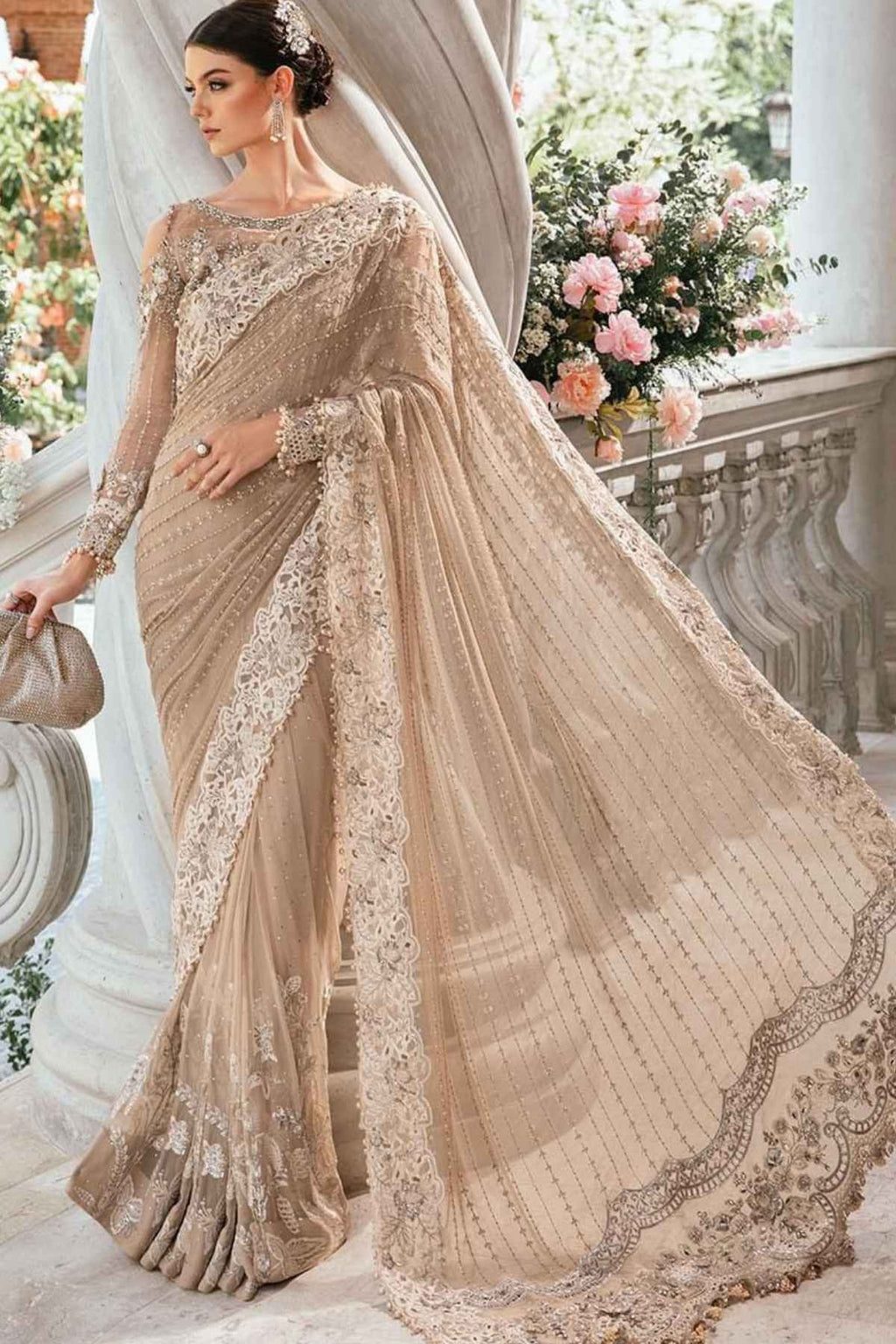 Woman in a beige saree with floral decorations on a balcony with flowers in the background