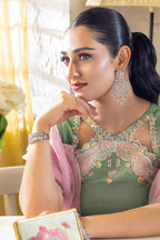 A woman with her hair in a ponytail is shown in a lifestyle setting, wearing a green embroidered traditional outfit with a pink dupatta and silver jewelry, including a large earring and bracelet.