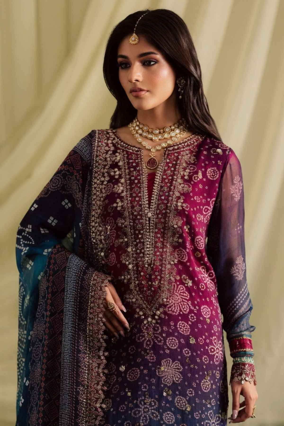 Woman wearing a traditional embroidered outfit with jewelry against a beige curtain background