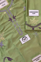 A close-up of an olive green embroidered fabric garment, showing the front bodice with purple and gold floral embroidery, a folded matching cuff with embroidered border, and fabric labels reading 'EMBROIDERED NECK,' 'EMBROIDERED CUFF,' and 'EMBROIDERED FRONT.'.
