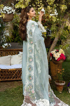 Woman in a light blue embroidered traditional outfit standing in a garden setting.