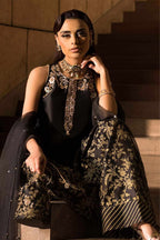A woman seated on stone stairs wearing an ornate black and gold embroidered traditional outfit with a matching dupatta, heavy gold jewelry, and a matching handbag.