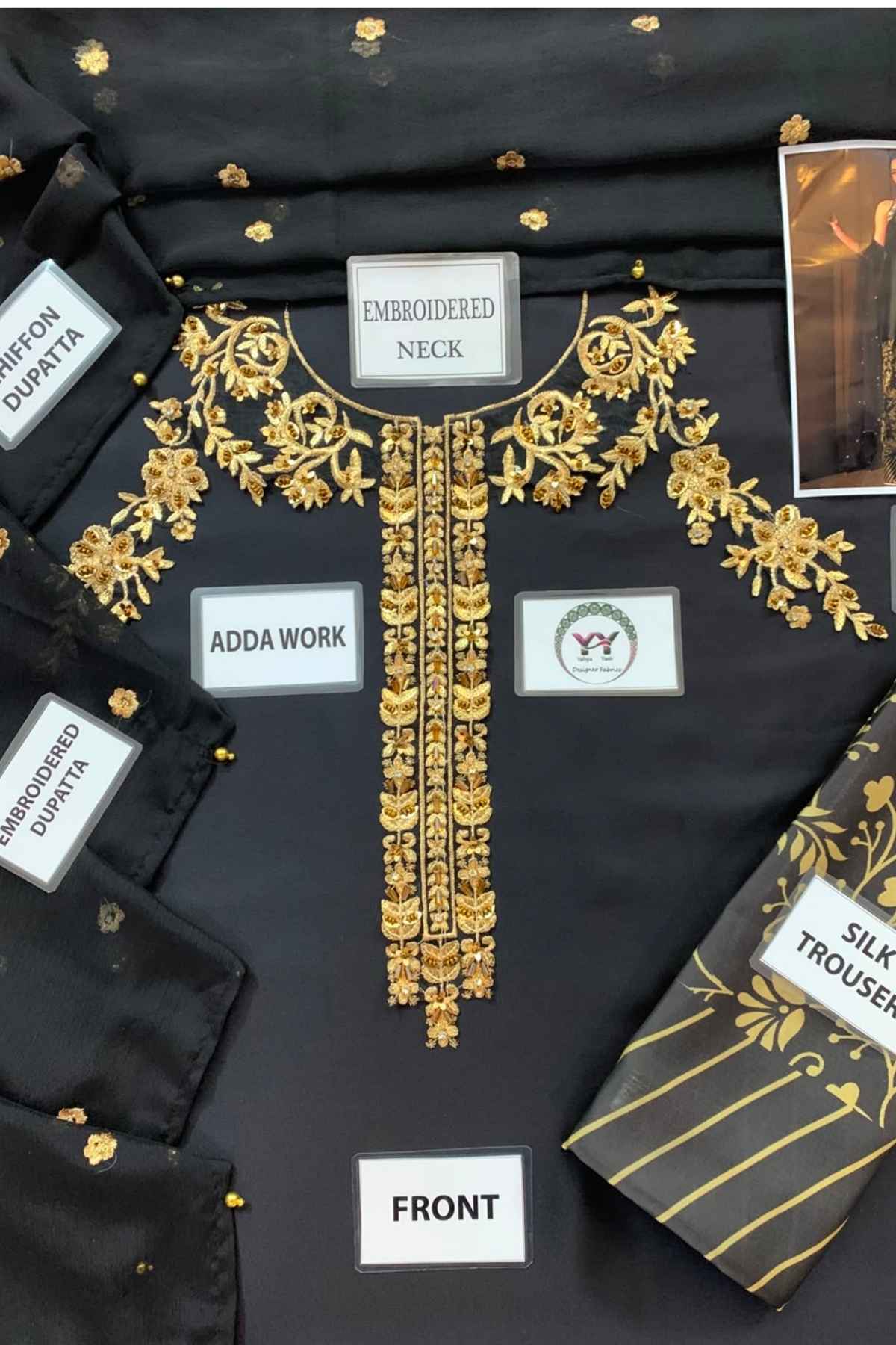 Black embroidered kurta laid flat with gold floral embroidery around the neckline and down the front placket. A matching black-and-gold silk trouser is partially visible at the lower right.