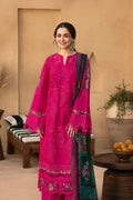 Woman wearing a bright pink embroidered traditional outfit with a green dupatta in an indoor setting.