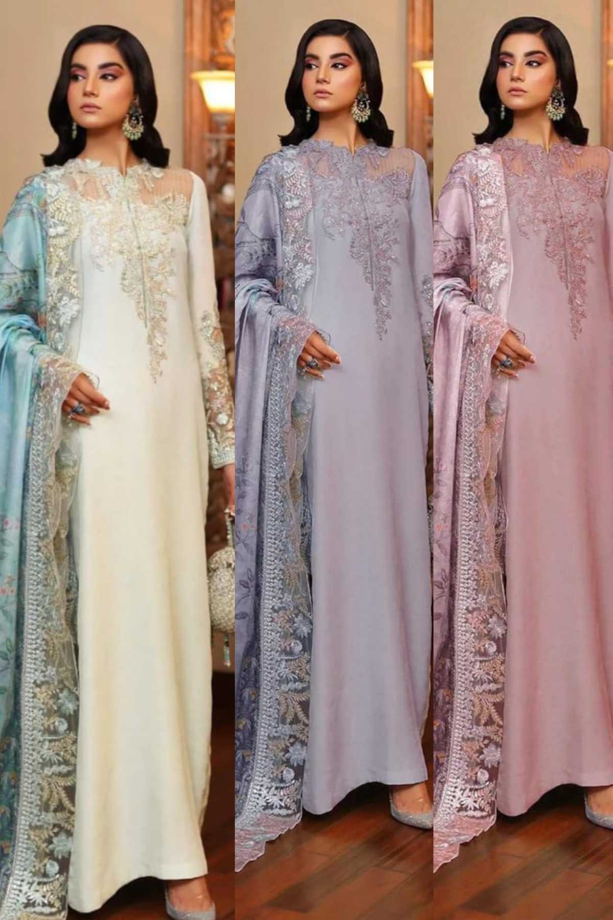 Three women modeling long, floor-length embroidered traditional dresses in different pastel shades: cream with light blue, lavender, and dusty pink. The dresses feature intricate floral embroidery and matching draped dupattas, set against an indoor background with warm lighting.